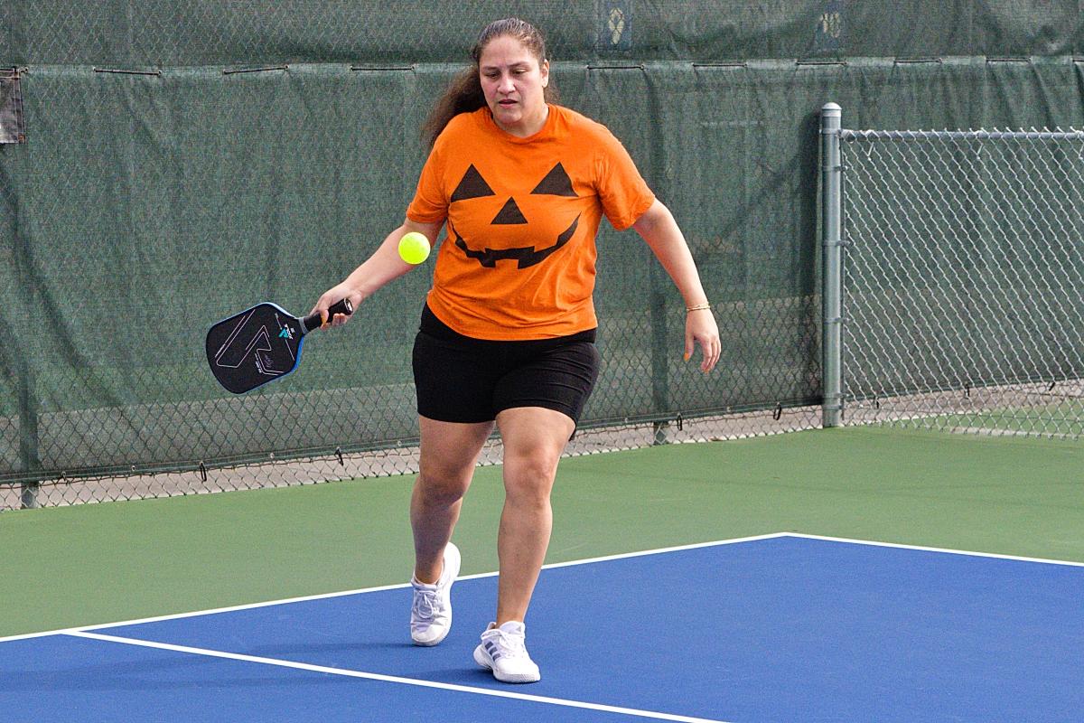 Woman in pumpkin shirt hits a forehand